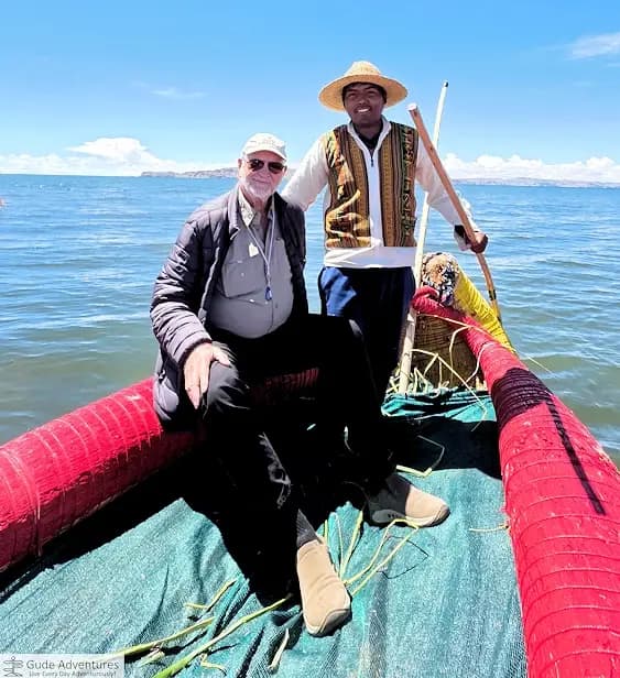 Leonard with the village chief in straw hat sitting on a red reed boat on Lake Titicaca.